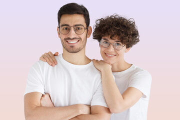 Wall Mural - Happy young couple embracing looking at camera on pink background