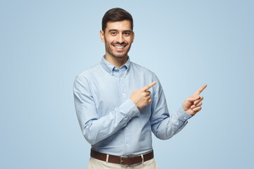 Wall Mural - Smiling young business man pointing away, isolated on blue background