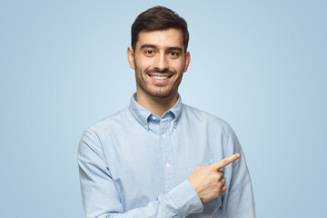 Smiling business man pointing right with index finger looking at camera on blue background