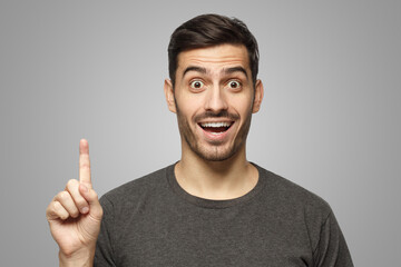 Wall Mural - Portrait of excited man looking at camera, smiling, pointing finger up if he has great idea