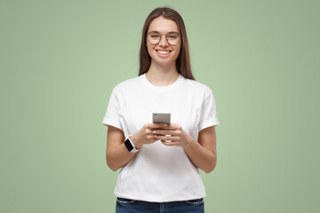 Wall Mural - Portrait of attractive young female in white t-shirt, holding smartphone, smiling at camera