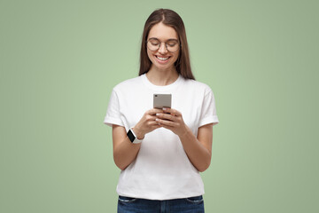 Wall Mural - Young attractive european female with smartphone in hands, isolated on green