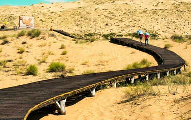 Wall Mural - Wooden pathway in the desert with people walking with umbrellas