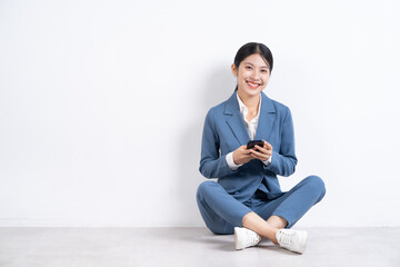 Canvas Print - Image of young Asian businesswoman sitting on floor and using smartphone