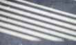The sun is casting railing shadow over the white concrete wall and floor.