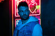 © Gonzalo - A young man fashionably dressed standing in the street at night. Illuminated signboards, neon, lights