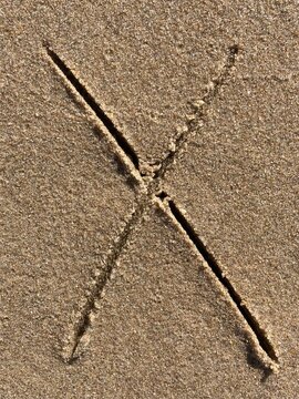 On the beach in the sand is carved the letter X