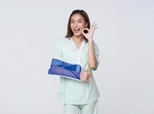 Asian Teenage Woman Wearing A Patient Gown Put On A Cast Due To Injury From An Accident Showing Hand Okay With An Impressive Smile.insurance Concept.