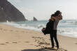 © LIGHTFIELD STUDIOS - bearded man lifting happy woman in hat and dress on beach near ocean.