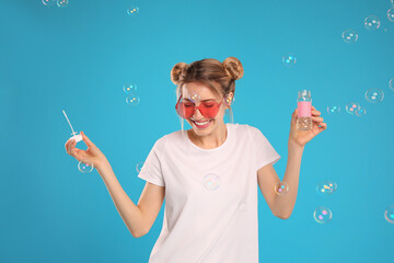 Young woman blowing soap bubbles on light blue background