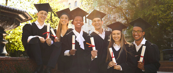 Wall Mural - Graduation. Portrait of joyful group of multiracial students who together received diploma of graduation and education. University friends in graduation gowns pose with diploma scrolls. Web banner.