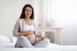 © Prostock-studio - Beautiful pregnant woman sitting on bed, holding glass of milk