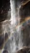 Vertical video in slow motion of a waterfall with a rainbow