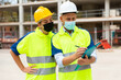 © JackF - Two qualified engineers in protective masks working on a construction site during a pandemic are discussing a construction ..plan, making important work notes