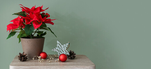 Wall Mural - Beautiful poinsettia plant in pot with Christmas decorations on table against green background with space for text