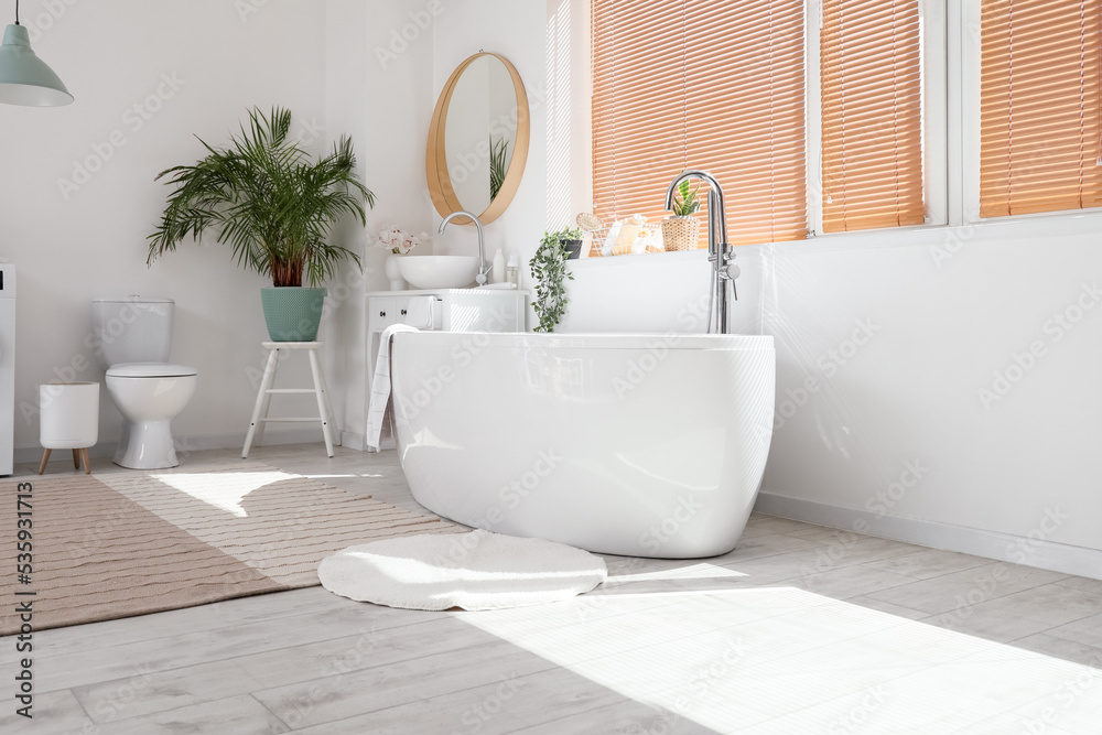 Interior of light bathroom with modern bathtub and houseplants