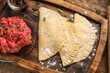 Board with raw chebureks, mince and spices on wooden background