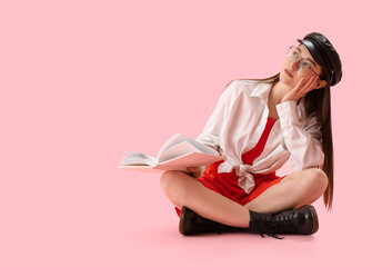 Wall Mural - Dreaming young woman with book sitting on pink background