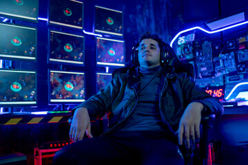 Caucasian gamer man sit with relax on chair and look forward with monitor of online game are in background. Concept of expert and professional of game and streaming for business.