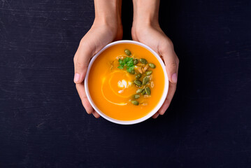 Wall Mural - Butternut squash pumpkin soup in bowl holding by hand on black background, Homemade food in autumn season, Top view