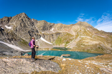 Wall Mural - The girl stands against the backdrop of mountain peaks and a blue lake. Beautiful mountain landscape for vacation, travel and healthy lifestyle