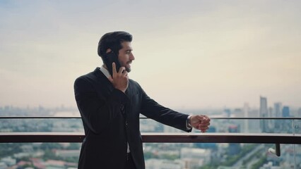 Handsome bearded startup businessman talking with partner by smartphone ,standing at the rooftop from office building , looking city view at the sunset