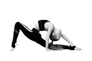 A young girl gymnast in a tracksuit does gymnastic stretching exercises. Black and white photo on a white background.