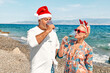 © Caterina Trimarchi - Funny adult couple wearing christmas costumes drinking sparkling wine and enjoying christmas vacations on tropical beach. Winter holiday concept.