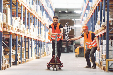 Wall Mural - Man riding trolley platform. Having fun. Two storage workers is in the warehouse