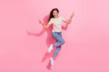 Poster - Full length photo of adorable shiny girl dressed beige t-shirt jumping high showing v-signs isolated pink color background