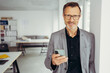 © contrastwerkstatt - smiling businessman using smart phone standing in office hallway, smiling male professional holding smartphone working with business apps texting sms enjoy corporate technology on mobile device
