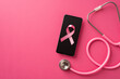 Breast cancer awareness concept. Top view photo of stethoscope and pink silk ribbon over smartphone on isolated pink background