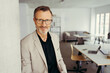© contrastwerkstatt - Smiling attractive mature man wearing glasses in modern office with copy space looking at the camera