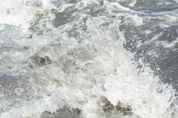 Close-up white water of the mountain stream in a summer day. White and grey foam of waves and drops of water