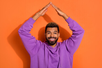 Wall Mural - Photo of funky nice dude boy model stylish pullover hold arms over head make house roof isolated on orange color background.