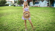 young thin skinny blonde girl stands on a green lawn in a summer dress and holds a straw hat