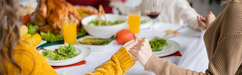 Wall Mural - Cropped view of family holding hands near thanksgiving dinner with turkey at home, banner