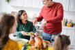 Senior man putting turkey on plate near interracial family celebrating thanksgiving at home