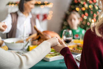 Wall Mural - multiethnic family holding hands and praying before christmas dinner on blurred background