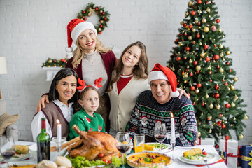 Wall Mural - happy multiethnic family looking at camera near delicious dinner and christmas tree