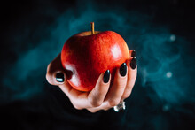 Woman As Witch Offers Red Apple - Symbol Of Toxic Proposal, Lure. Fairytale, White Snow, Wizard Concept. Halloween Celebration, Cosplay. Smoke, Mist Background.