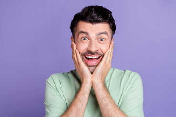 Wall Mural - Portrait of crazy impressed positive man with brunet hairdo dressed t-shirt hands on cheekbones isolated on purple color background