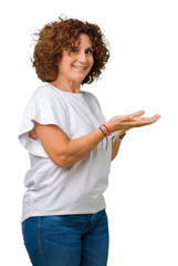 Wall Mural - Beautiful middle ager senior woman wearing white t-shirt over isolated background Pointing to the side with hand and open palm, presenting ad smiling happy and confident