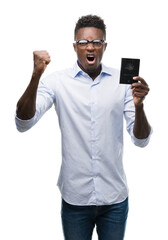 Canvas Print - Young african american man holding australian passport annoyed and frustrated shouting with anger, crazy and yelling with raised hand, anger concept