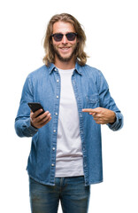 Canvas Print - Young handsome man with long hair over isolated background sending message using smartphone very happy pointing with hand and finger