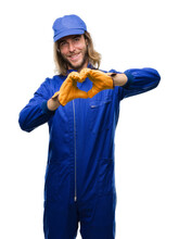 Young Handsome Mechanic Man With Long Hair Over Isolated Background Smiling In Love Showing Heart Symbol And Shape With Hands. Romantic Concept.