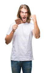 Sticker - Young handsome man with long hair eating chocolate bar over isolated background annoyed and frustrated shouting with anger, crazy and yelling with raised hand, anger concept