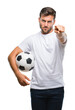 © Krakenimages.com - Young handsome man holding soccer football ball over isolated background pointing with finger to the camera and to you, hand sign, positive and confident gesture from the front