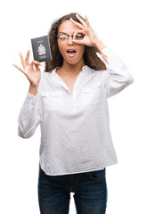 Wall Mural - Young hispanic woman holding passport of Canada with happy face smiling doing ok sign with hand on eye looking through fingers