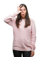 Sticker - Young beautiful hispanic woman wearing a sweater doing ok gesture shocked with surprised face, eye looking through fingers. Unbelieving expression.